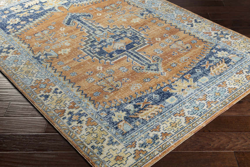 Close-up of the Trotters Orange/Blue Performance Rug showing its bohemian-inspired design and rich brick red, brown, and navy colors. Corner