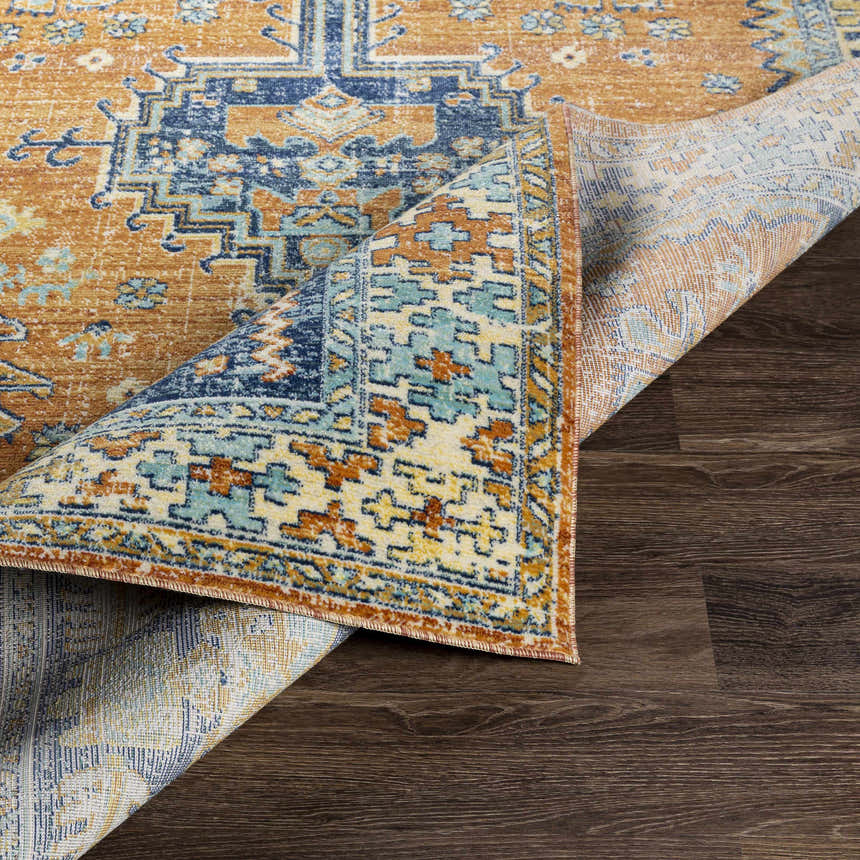 Close-up of the Trotters Orange/Blue Performance Rug showing its bohemian-inspired design, colors, and texture on a wood floor. Fold