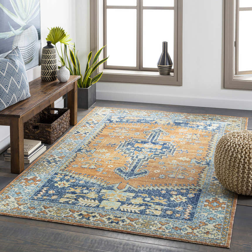 Living room scene with Trotters Orange/Blue Performance Rug, wood bench, woven pouf, and natural light. Bohemian style. Roomscene-Rectangle