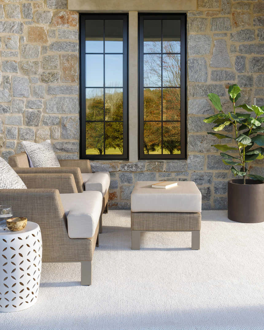 Outdoor patio scene with Zareh Off White Solid Area Rug, neutral chairs, stone wall, and black framed windows. Roomscene-Rectangle