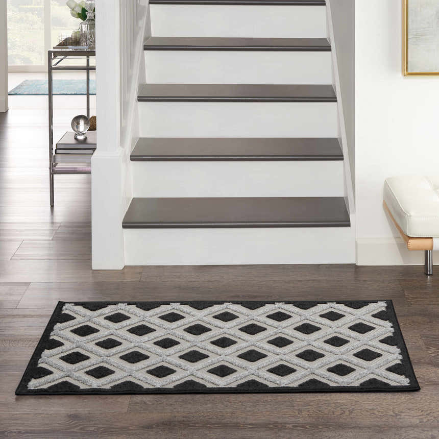 Entryway with Nourison Aloha Black White Modern Area Rug runner, diamond pattern, dark wood floors, and white stairs.