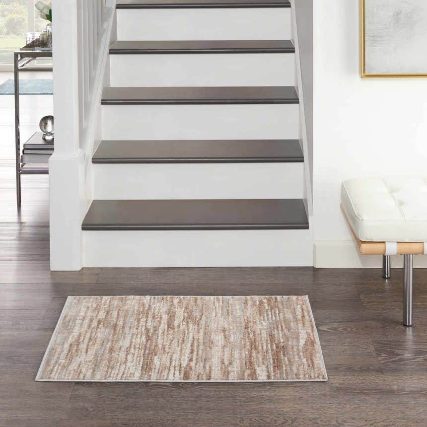 Entryway with Nourison Elation Ivory Grey rug on dark wood floor, white stairs, and modern bench.