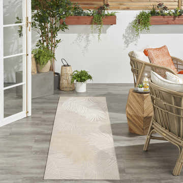 Patio scene with rattan chairs and a beige Nourison Suncoast Tropical Area Rug runner featuring a palm leaf design.