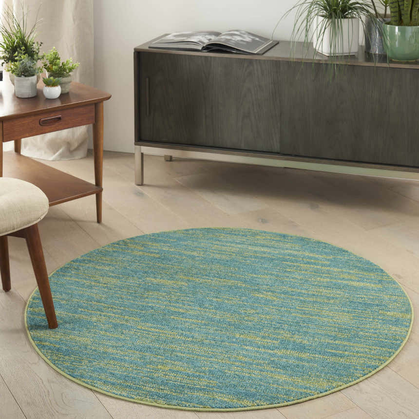 Living room scene with round Nourison Essentials Blue Green Outdoor Area Rug, wood floors, and mid-century modern furniture.
