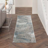 Hallway with Nourison Rustic Textures Light Grey Blue rug, wood floors, silver console table, and white walls.