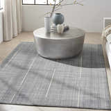 Living room scene with denim Calvin Klein CK041 Architectura rug, round metal coffee table, and neutral decor.