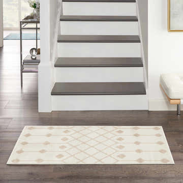 Entryway scene with a Nourison Grafix Ivory Beige rug on dark wood floors, stairs, and a white bench.