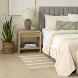 Bedroom scene with a Nourison Positano beige ivory rug, wood nightstand, snake plant, and neutral bedding.
