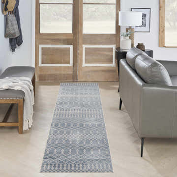 Entryway with Nourison Astra Blue Bohemian Runner Rug, gray leather sofa, wood door, and light wood floors.