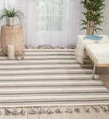 Bright room scene with Nourison Rio Vista Ivory/Grey rug, striped pattern, tassels, white bench, and houseplants.
