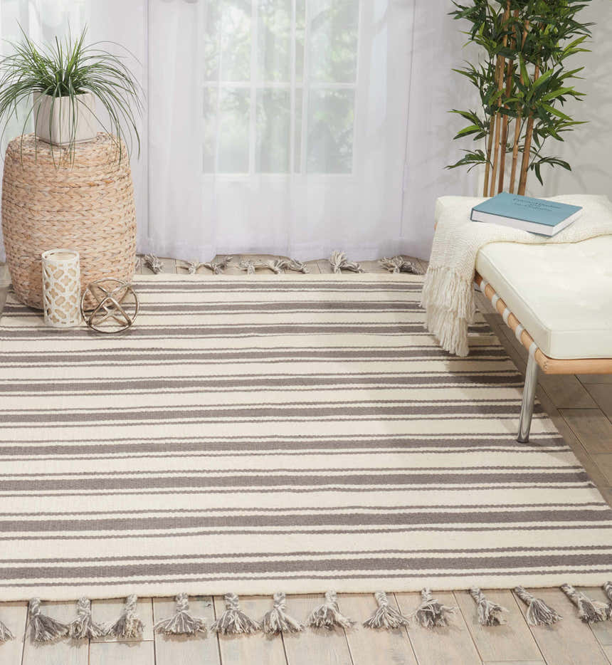 Bright room scene with Nourison Rio Vista Ivory/Grey rug, striped pattern, tassels, white bench, and houseplants.