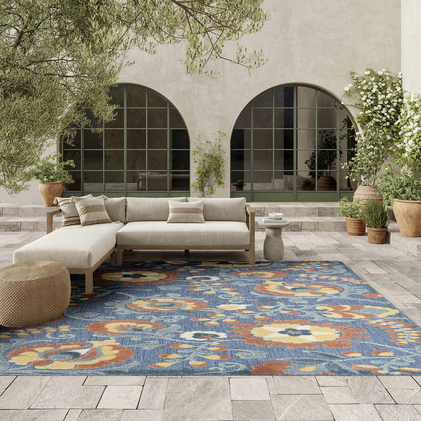Outdoor patio scene with a Nourison Aloha Blue Rose rug, beige sectional sofa, and potted plants.