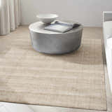 Minimalist living room with a beige Calvin Klein CK043 Spun rug, round coffee table, and light wood floors.