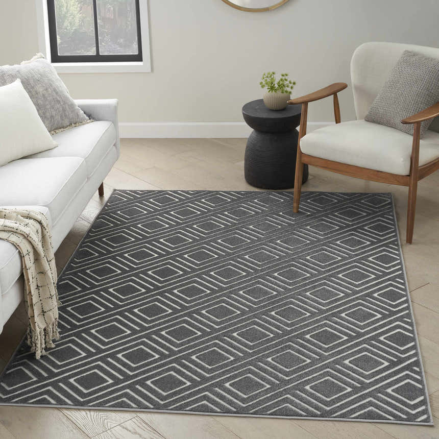 Living room scene with a grey geometric Nourison Care Free rug, white sofa, wood chair, and modern side table.