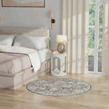 Bedroom scene with round Nourison Oushak Home Charcoal Vintage rug, taupe tones, and natural light.