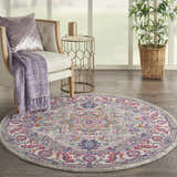 Living room scene with round Nourison Passion Light Grey Pink rug, chair, side table, and plant near a window.