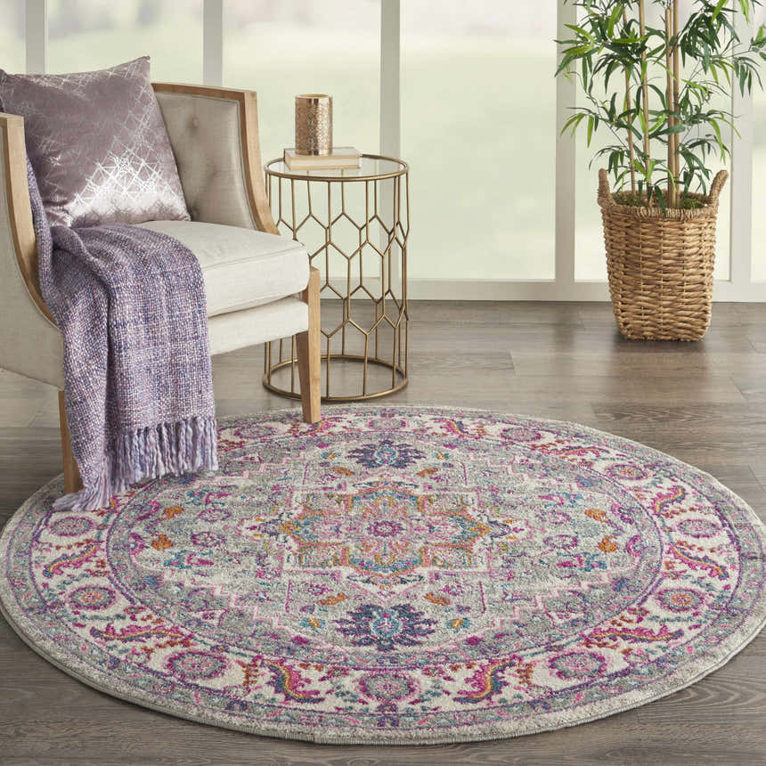 Living room scene with round Nourison Passion Light Grey Pink rug, chair, side table, and plant near a window.