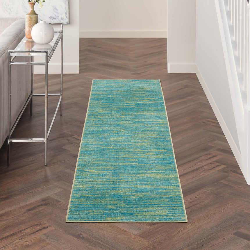 Hallway scene with Nourison Essentials Blue Green Outdoor Area Rug on herringbone wood floor.