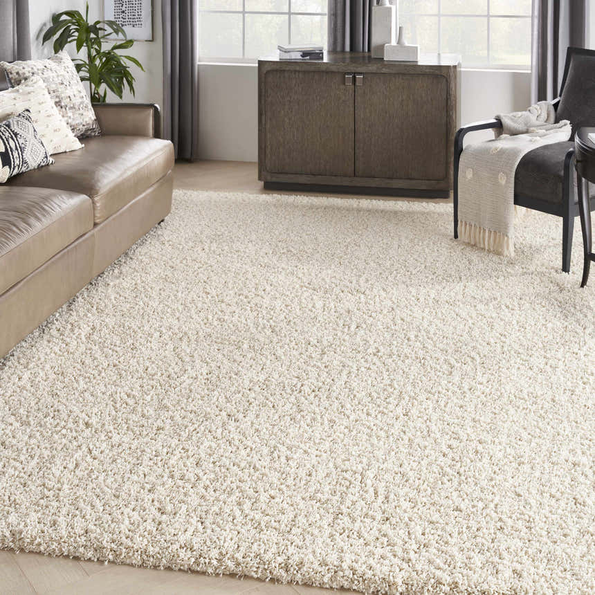 Living room scene with a cream Nourison Amore shag rug, tan leather sofa, gray cabinet, and chair. Neutral, cozy vibe.