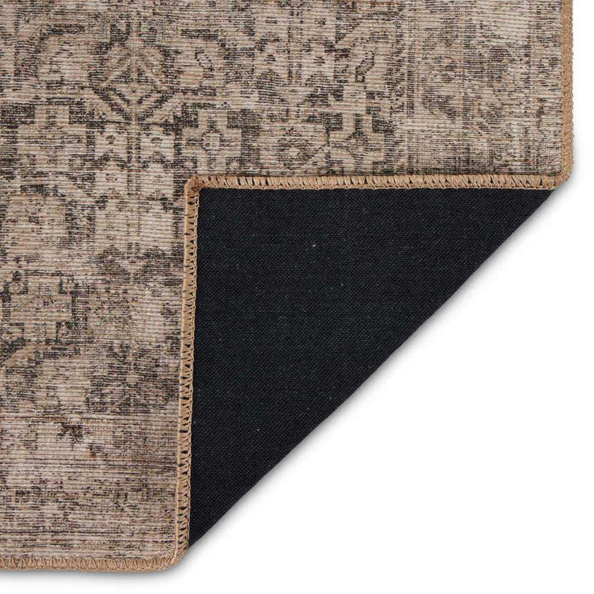 Close-up of the Four Hands Priya Area Rug showing its camel, light beige, and tan traditional pattern and black backing. Fold