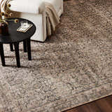 Living room scene with a Four Hands Priya Area Rug in camel, light beige, and tan under a modern side table and cream chair. Styleshot