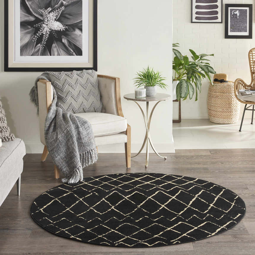 Living room scene with a round Nourison Grafix Black Bohemian rug, chair, side table, and plants for a cozy, modern look.