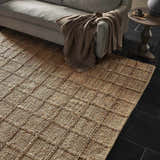 Living room scene with a Four Hands Grid Jute Rug, natural sofa, throw blanket, and dark stone tile flooring. Styleshot