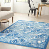 Living room scene with Waverly Sun N' Shade Blue Tropical Area Rug, beige armchair, wood table, and dining set.