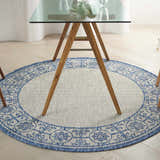 Dining room with a round Nourison Country Side Ivory Blue rug under a glass table.