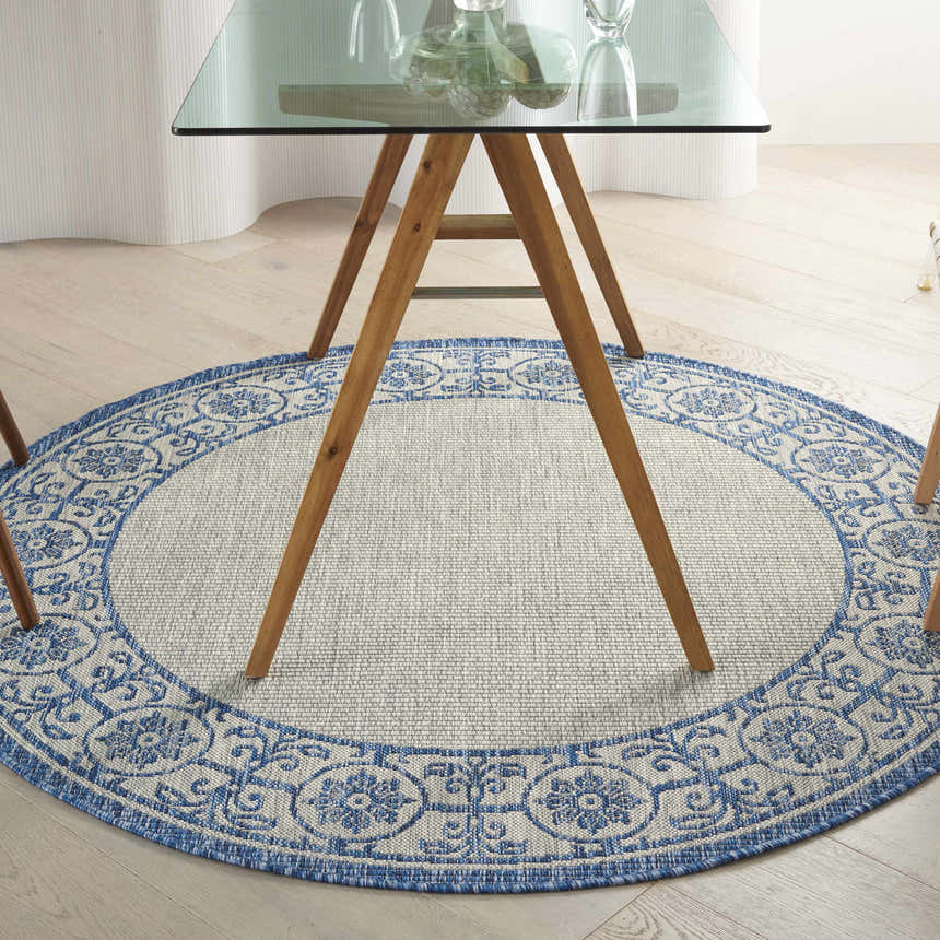 Dining room with a round Nourison Country Side Ivory Blue rug under a glass table.