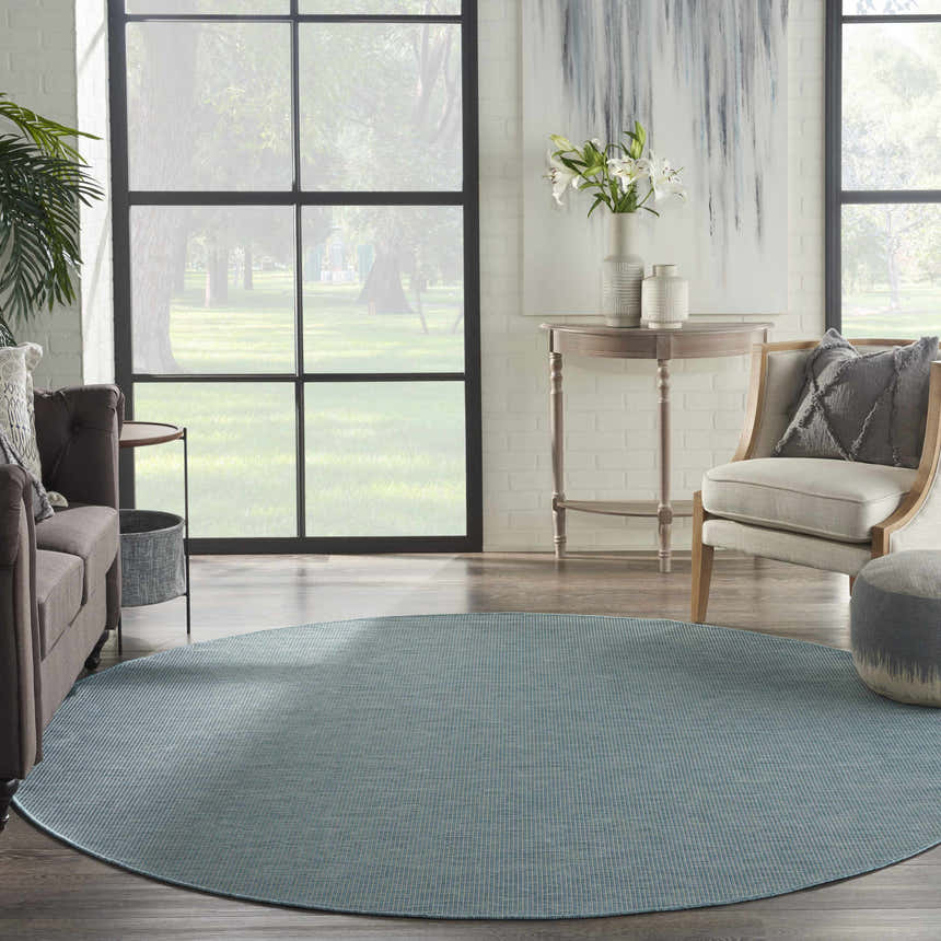 Living room scene with a round Nourison Positano Aqua rug, gray sofa, chair, and table. Large window with a view.
