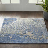 Entryway with a Nourison Prismatic Denim rug, featuring a blue abstract pattern on dark wood floors. Plant and white doors.