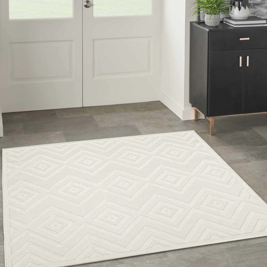 Entryway with a Nourison Versatile Ivory White Modern Area Rug, white door, gray tile floor, and black cabinet.