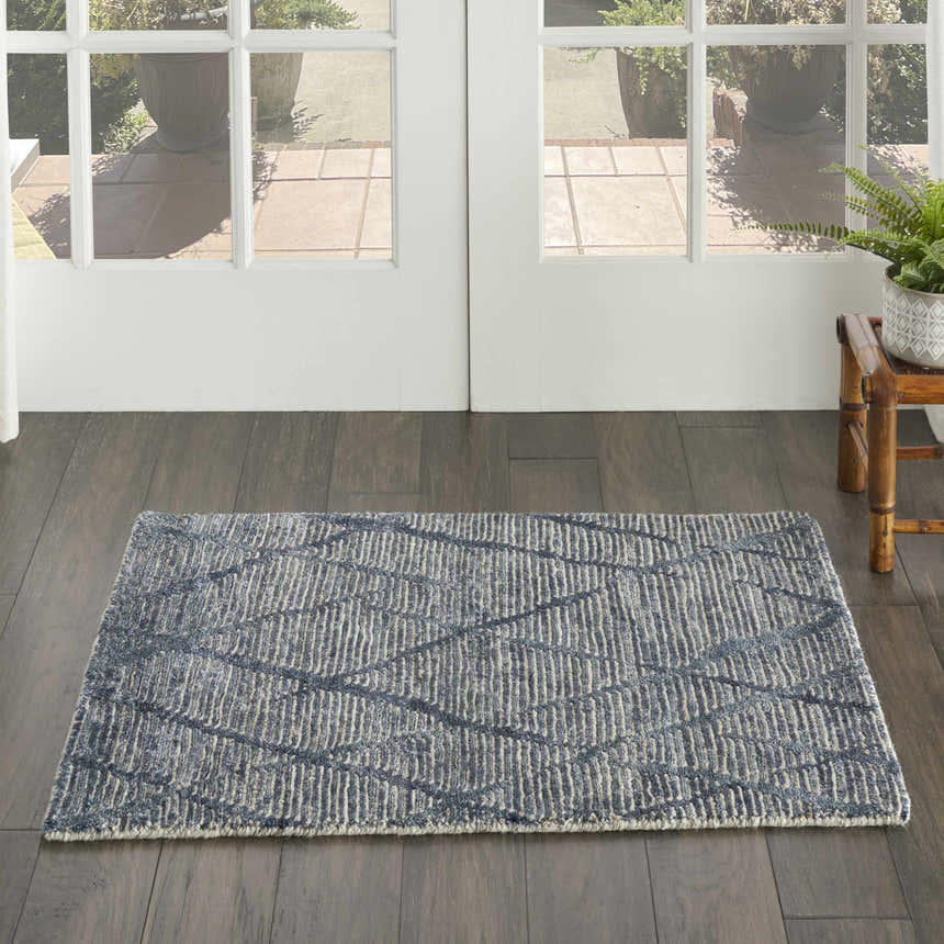 Entryway scene with a Nourison OCEAN Indigo rug. Purple, mid-century modern rug on dark wood floors near a white door.