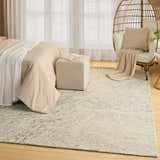 Neutral bedroom scene with a DKNY Pure Angles Grey rug, bed, ottoman, and rattan chair.