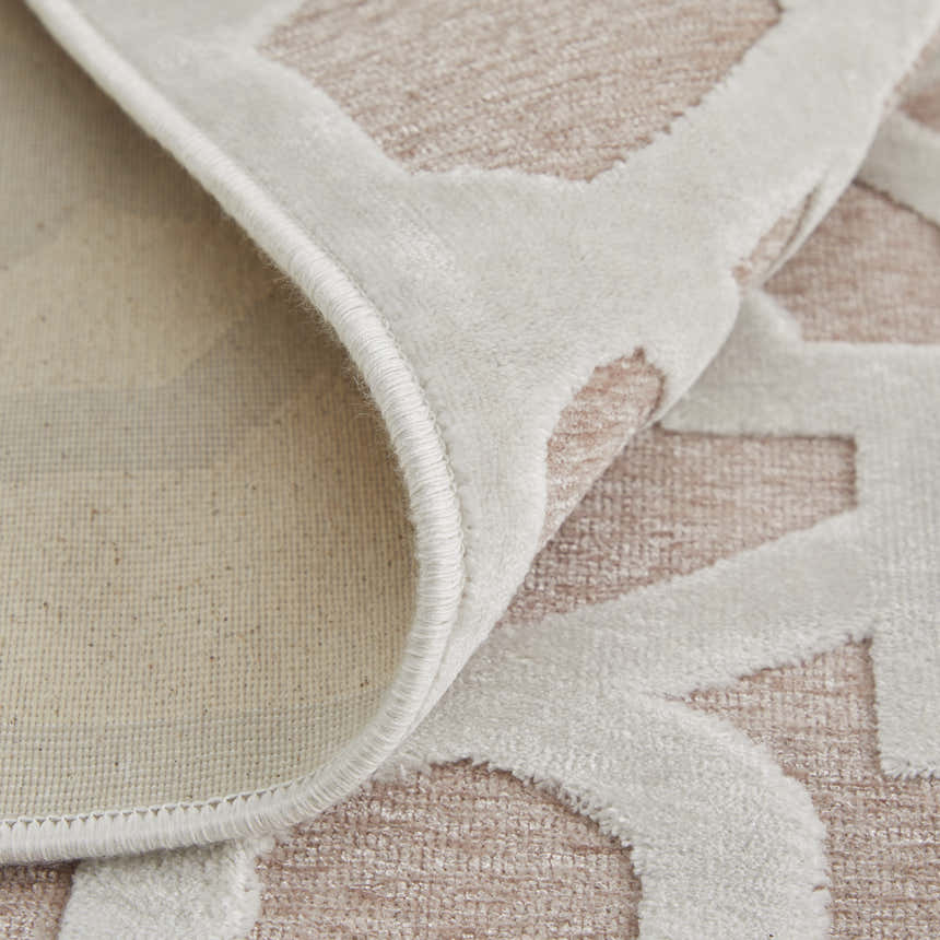 Close-up of Feizy Saphir Mira rug. Pink and white interlocking geometric diamond pattern, showing texture and backing. Fold