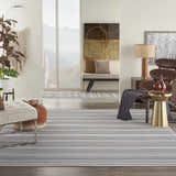 Living room scene with a Nourison Key Largo Blue Contemporary Area Rug, striped, with a chair, ottoman, and neutral decor.