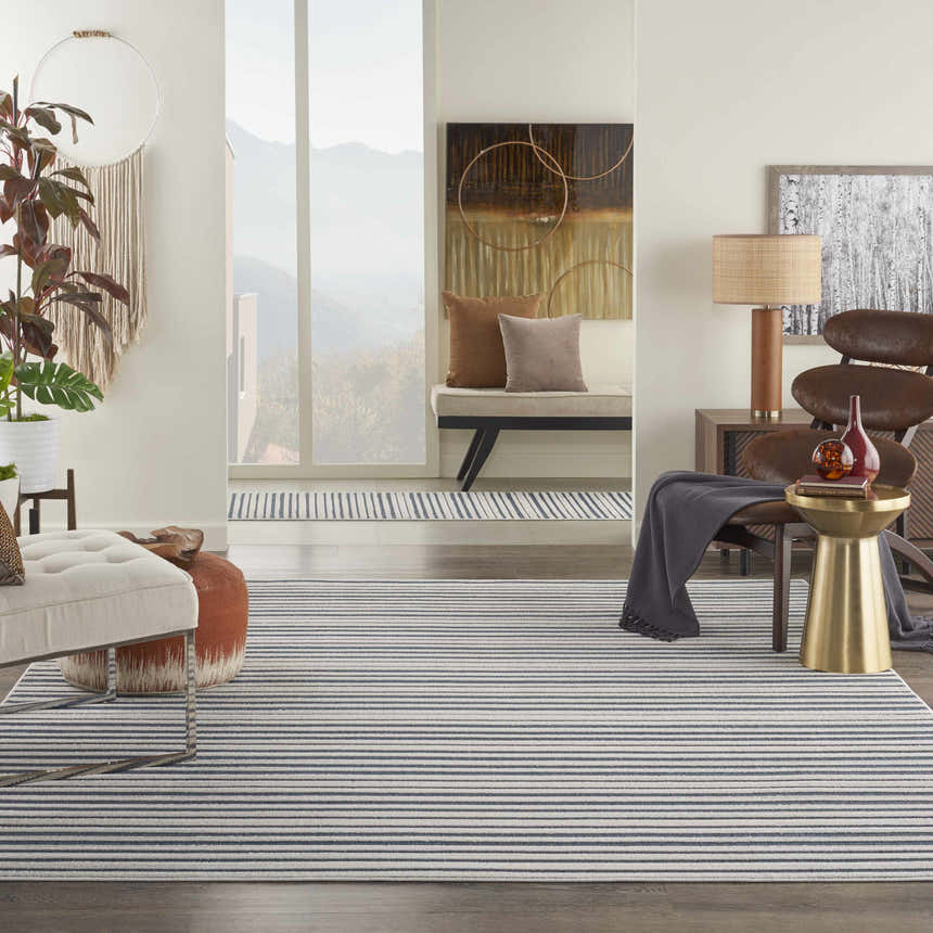 Living room scene with a Nourison Key Largo Blue Contemporary Area Rug, striped, with a chair, ottoman, and neutral decor.