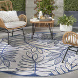 Outdoor patio scene with a round Nourison Aloha Ivory Navy Tropical Area Rug, wicker chairs, and a small table.