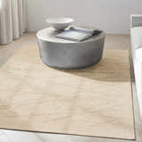 Minimalist living room with a Calvin Klein CK044 Wander Natural rug, round concrete table, and light wood floors.