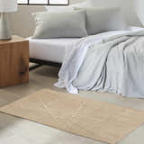 Bedroom scene with Calvin Klein CK044 Wander Natural rug, wood nightstand, and gray bedding. Modern, neutral style.