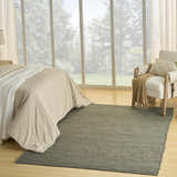 Farmhouse bedroom with a Nourison Natural Jute Sage rug, linen bedding, and a view of a lush green landscape.