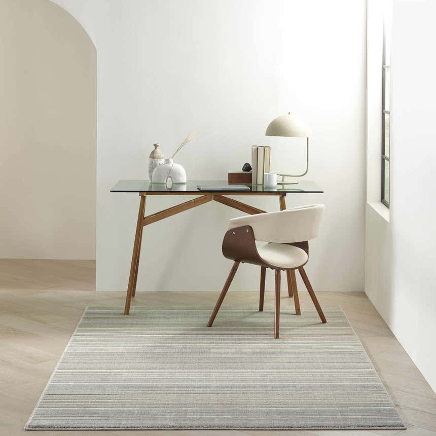 Minimalist office with Nourison Marmara Grey Ivory Teal Rug, glass top desk, and modern chair.