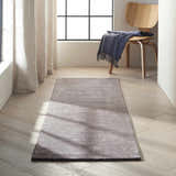 Hallway scene with a Calvin Klein Home Ravine Nightshade rug, wood floors, light curtains, and a modern wood chair.