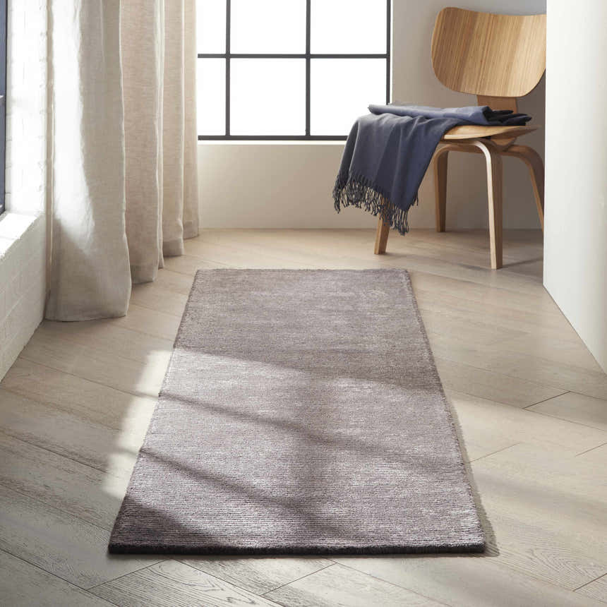 Hallway scene with a Calvin Klein Home Ravine Nightshade rug, wood floors, light curtains, and a modern wood chair.