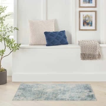 Bright entryway with Nourison Astra Blue Ivory rug, pillows, throw, art, and plant.