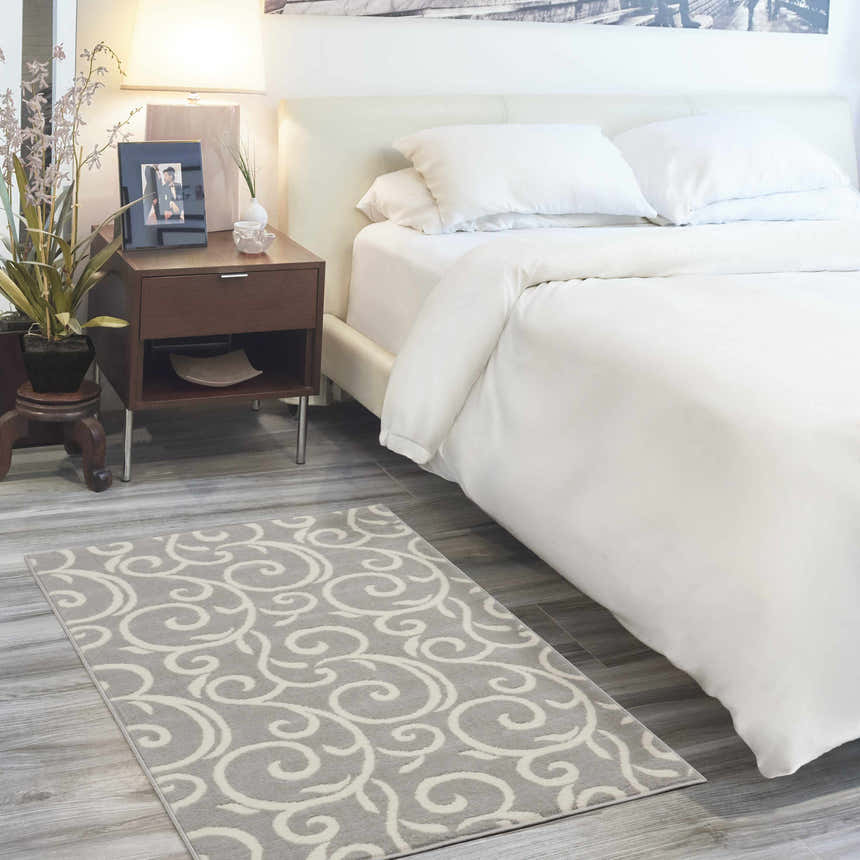 Bedroom scene with a Nourison Grafix Grey rug, white bedding, and wood nightstand. Contemporary style.