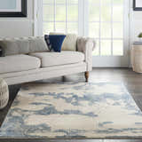 Living room scene with a Nourison Etchings Ivory/Light Blue rug, cream sofa, and dark wood floors. Modern style.