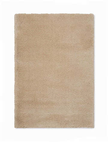 Close-up of a plush, machine-made Calvin Klein Brooklyn beige area rug. The shag rug has a soft, neutral tone.