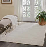 Sunlit room with Nourison OCEAN Pearl rug, bench, and plant. Neutral tones create a serene, modern space.